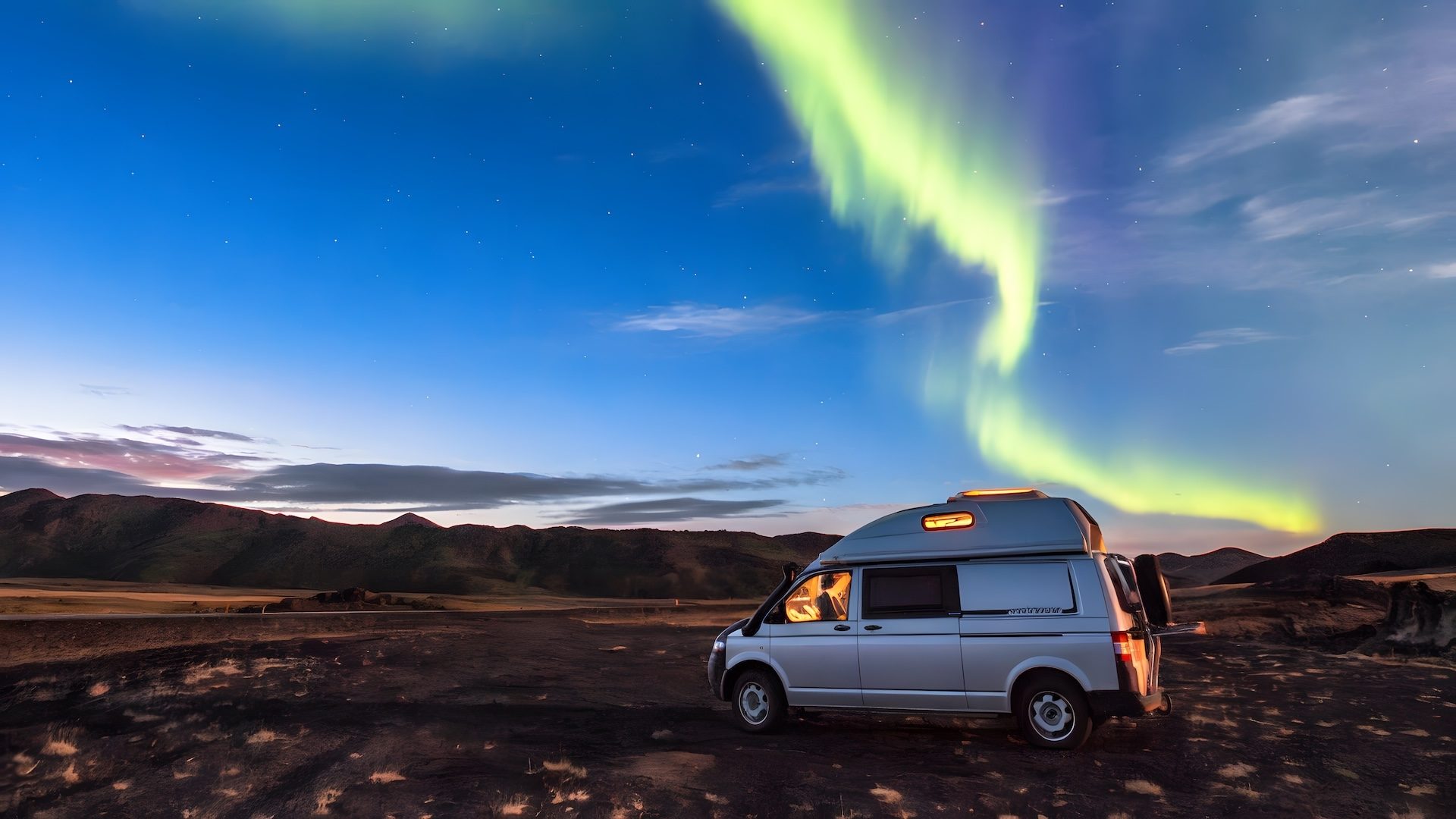 Campmobil Van auf einer Schotterstraße vor der Auora Borealis